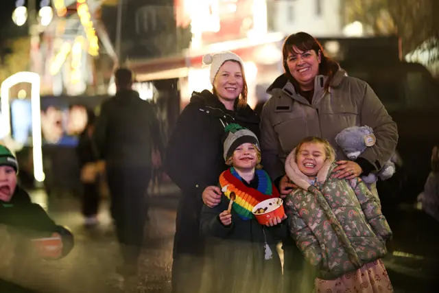Two adults and two children smiling together beneath the lights at Christmas Town