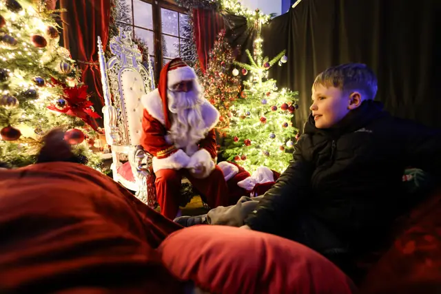 A family visiting Santa in the Christmas Town Grotto, surrounded by Christmas trees and warm lights