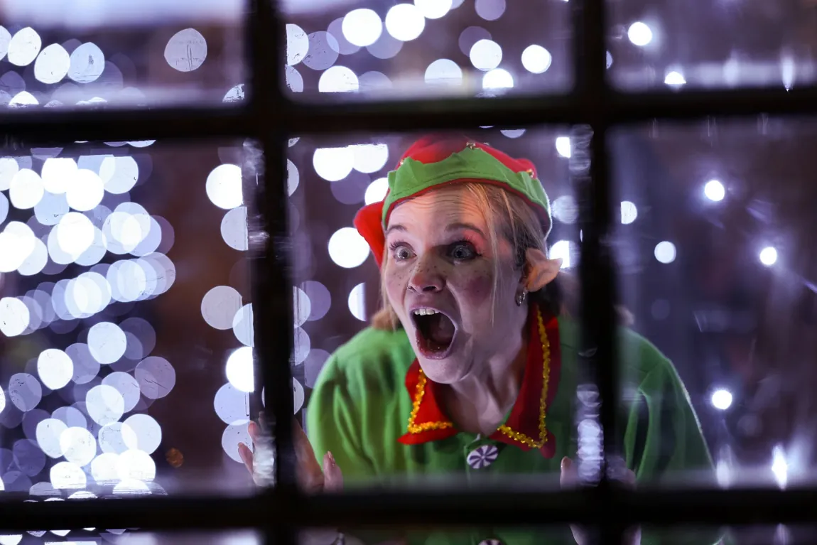An excited Christmas Town elf looking through a window surrounded by sparkling lights